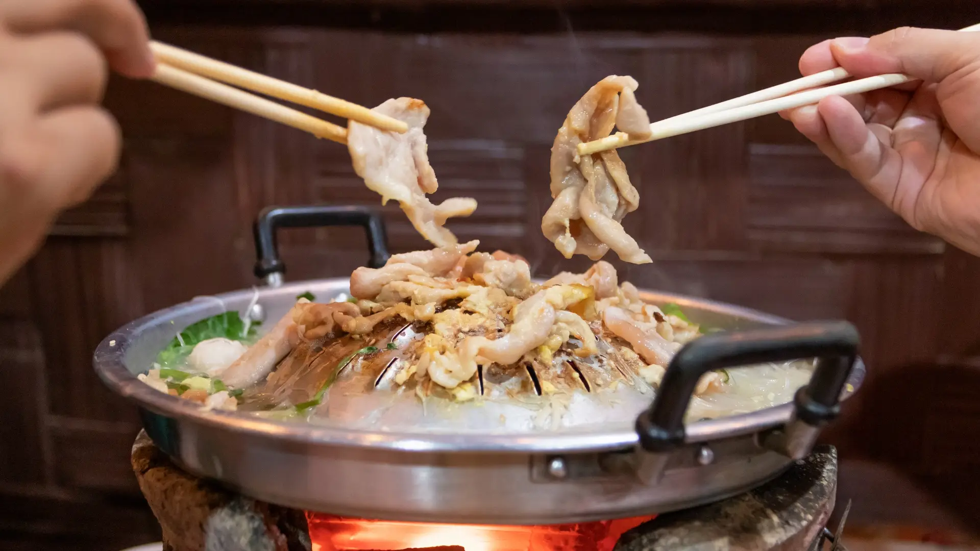 การคีบชิ้นหมูบนเตาหมูกะทะ สื่อถึงรสชาติอูมามิและความอร่อยของหมูกะทะที่มีการใช้ผงชูรสเสริมรสชาติอร่อย ถูกปาก